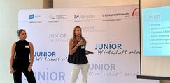 zwei junge Frauen stehen auf einer Bühne und halten eine Präsentation.