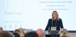 Anna Stolz Eine Rednerin steht lächelnd an einem Pult und spricht vor einem Publikum. Im Hintergrund ist eine Projektion mit der Aufschrift „Seminar Preisträger 2024“ zu sehen.