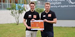 Zwei junge Männer posieren für ein Foto und halten eine Urkunde in der Hand.