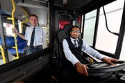 Ein Mann sitz am Steuer eines Busses, ein anderer Mann steht neben ihm im Bus. 