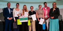 Vier Schülerinnen posieren mit Urkunden und Geschenken für ein Foto. Dabei sind sie von drei Erwachsenen, einem Mann und zwei Frauen, umringt.