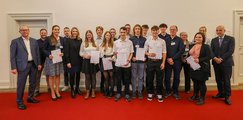 Gymnasium München-Trudering Die Schülerinnen und Schüler stehen gemeinsam mit Lehrern und Preisverleihern auf einem roten Teppich und halten ihre Preise in die Kamera.