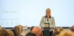 bbw-Vorstandsvorsitzende Sandra Stenger Eine Rednerin steht lächelnd an einem Pult und spricht vor einem Publikum. Im Hintergrund ist eine Projektion mit der Aufschrift „Seminar Preisträger 2024“ zu sehen.