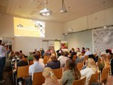 Menschen sitzen in einem Vorlesungsraum und hören einem Dozenten zu