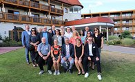 Eine Gruppe Menschen steht auf einer Wiese zusammen vor einem großen Gebäude.
