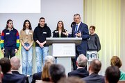 Ein Mann hält auf einer Bühne vor einer Gruppe Schülern eine Rede.