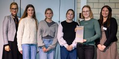 Frauen und Schülerinnen posieren für ein Foto. Eine Person hält eine Auszeichnung in der Hand.