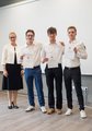 Drei Schüler stehen nebeneinander und halten eine Urkunde in die Kamera. Links neben ihnen steht eine Frau und lächelt in die Kamera.