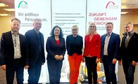 Eine Gruppe von sieben Leuten steht zusammen vor einer bfz und bbw Bildschirmanzeige.