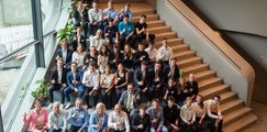 Eine Gruppe aus Schüler*innen und Erwachsenen sitzen auf einer Treppe, zeigen Daumen ab und lachen nach oben in die Kamera.