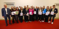 Johannes-Gutenberg-Gymnasium Waldkirchen Eine Gruppe von Personen posiert auf einem roten Teppich für ein Gruppenfoto. Einige halten Zertifikate in den Händen, während sie lächeln. Im Hintergrund stehen weitere Teilnehmer und Organisatoren.