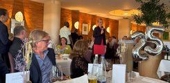 Eine Frau steht mit Mikrofon in der Hand in einem voll besetzten Restaurant und hält eine Rede.