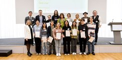 Gymnasium Geretsried Eine Gruppe Jugendlicher steht gemeinsam mit ihrer Lehrkraft auf der Bühne und hält Urkunden und einen Preis in den Händen.