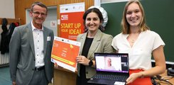 Ein Mann posiert neben zwei Frauen für ein Foto. Die eine hält eine Urkunde, die andere einen Laptop in der Hand.