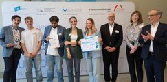 Die Schüler*innen des Fachakademie für Ernährungs- und Versorgungsmanagement München Fünf Schüler*innen stehen mit drei Erwachsenen vor einer Leinwand. Die Jugendlichen halten zwei Urkunden in den Händen.