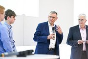 Ein Mann hält eine Rede. Zwei weitere Männer schauen in dabei an.