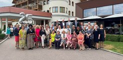 Eine Gruppe von Menschen posiert vor einem Hotel für ein Foto. Im Hintergrund sieht man Luftballons in der Form der Zahl 25.