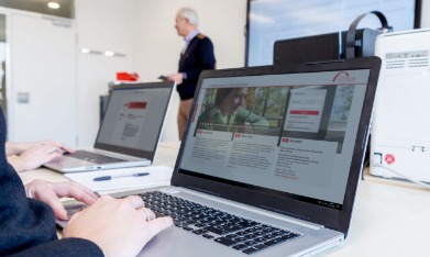 Ein Mann hält einen Vortrag, Schüler*innen sitzen an Laptops vor ihm. 