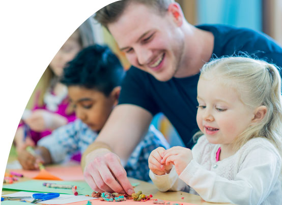 Ein junger Mann bastelt mit Kindergartenkindern. 