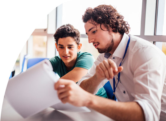 Ein junger Mann und ein Schüler schauen sich gemeinsam ein Aufgabenblatt an.