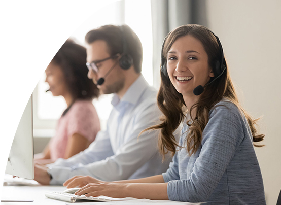 Qualifikation von an- und ungelernten Mitarbeiter*innen Eine Frau mit Headset sitzt vor einem Pc und lächelt in die Kamera.
