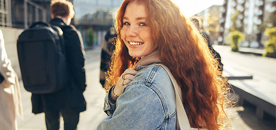 Eine junge Studentin lächelt in die Kamera. Im Hintergrund sind weitere Studenten von hinten zu sehen.