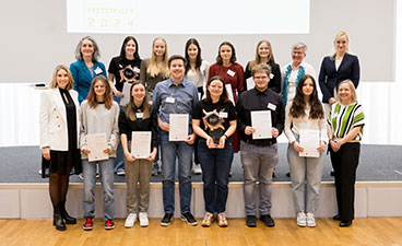 Das Annette-Kolb-Gymnasium Traunstein Schülerinnen und Schüler stehen mit ihren Lehrkräften vor der Bühne und halten ihre Urkunden und den Preis hoch.