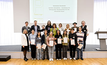 Gymnasium Geretsried Eine Gruppe Jugendlicher steht gemeinsam mit ihrer Lehrkraft auf der Bühne und hält Urkunden und einen Preis in den Händen.