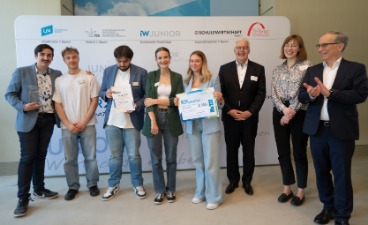 Die Schüler*innen des Fachakademie für Ernährungs- und Versorgungsmanagement München Fünf Schüler*innen stehen mit drei Erwachsenen vor einer Leinwand. Die Jugendlichen halten zwei Urkunden in den Händen.