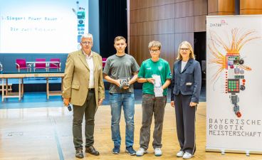 Schüler der Staatlichen Realschule Schonungen mit dem Team "Die zwei Rabauken" Zwei Jugendliche, ein Mann und eine Frau posieren samt Auszeichnung für ein Foto.