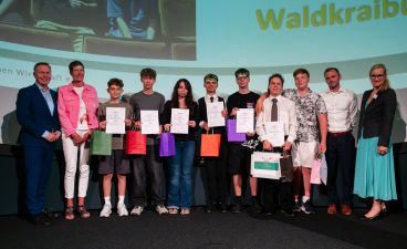 Eine Gruppe von Schülern posiert, umringt von vier Erwachsenen, mit Urkunden in der Hand für ein Foto.