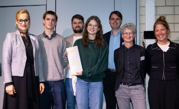 Mehrere Erwachsene sowie eine Schülerin und ein Schüler posieren für ein Foto. Die Schülerin hat eine Auszeichnung in der Hand. Mehrere Erwachsene sowie eine Schülerin und ein Schüler posieren für ein Foto. Die Schülerin hat eine Auszeichnung in der Hand.