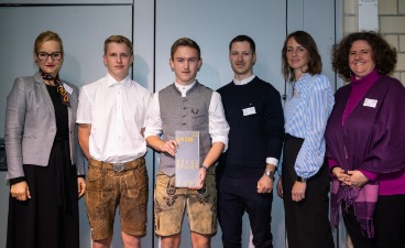 Mehrere Erwachsene posieren mit zwei Schülern für ein Foto. Ein Schüler hält eine Auszeichnung in den Händen. Mehrere Erwachsene posieren mit zwei Schülern für ein Foto. Ein Schüler hält eine Auszeichnung in den Händen.