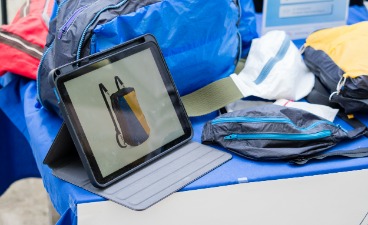 Auf einem Tisch stehen Taschen aus recyceltem Gleitschirmstoff sowie ein Tablett mit einer Animation.