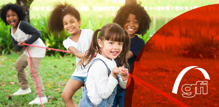 Vier Kinder spielen Tauziehen und lachen dabei.