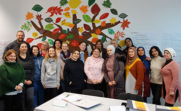 Eine Gruppe Frauen und ein Mann stehen zusammen vor einer gebastelten Abbildung eines Baumes. Sie lächeln in die Kamera.
