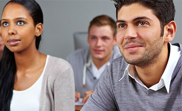Klassenzimmersytuation: Zwei Männer und eine Frau schauen nach vorne an die Tafel. 