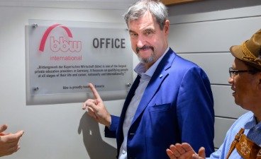 Dr. Markus Söder, Bayerischer Ministerpräsident, zeigt auf das Schild des neuen bbw-Projektbüros in Kapstadt. Er ist umringt von applaudierenden Menschen.
