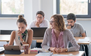Mehrere Studierende sitzen mit Tablet und Laptop an Tischen.