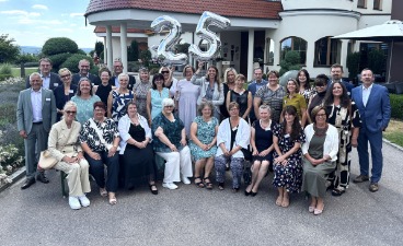 Eine Gruppe von Menschen posiert vor einem Hotel. Luftballons zeigen die Zahl 25 an.