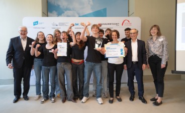Die Schüler*innen der Rudolf-Steiner-Schule Gröbenzell Eine Gruppe von Schüler*innen stehen gemeinsam mit vier Erwachsenen vor einer Leinwand und halten zwei Urkunden in der Hand.