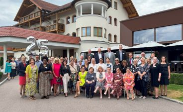Eine Gruppe von Menschen posiert vor einem Hotel. Über den Menschen sind Luftballons in Form der Zahl 25 zu sehen.