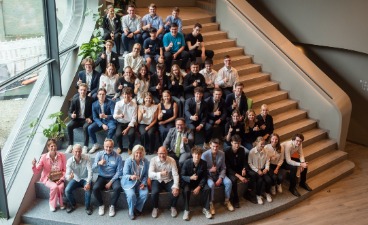 Eine Gruppe aus Schüler*innen und Erwachsenen sitzen auf einer Treppe, zeigen den Daumen nach oben und schauen dabei in die Kamera.
