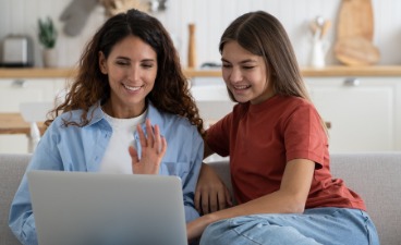 Zwei weibliche Personen sitzen auf einem Sofa und sehen gemeinsam in einen Laptop.