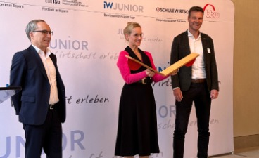 Eine Frau steht in der Mitte von zwei Männern und klappt eine Startklappe zusammen.