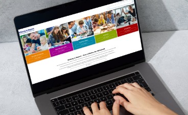 Hände tippen auf einem Laptop, auf dessen Bildschirm eine Website mit farbigen Kacheln und Bildungsbildern angezeigt wird.