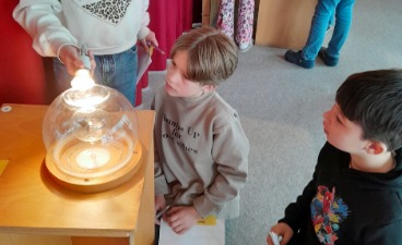 Zwei Kinder beobachten fasziniert ein Experiment mit einer leuchtenden Glaskugel in einem Raum.