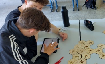 Zwei Jugendliche arbeiten im Workshop „Energy4Future“ an einem Tisch mit einem Tablet und sechseckigen Holzbausteinen eines Planspiels zur modernen Stromversorgung.