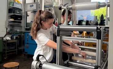 Eine Jugendliche bedient gemeinsam mit einem Betreuer eine Rollenmaschine zur Folienverarbeitung.