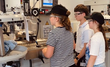 Zwei Mädchen mit Schutzbrillen stehen an einer großen Fräsmaschine in einer Lehrwerkstatt.